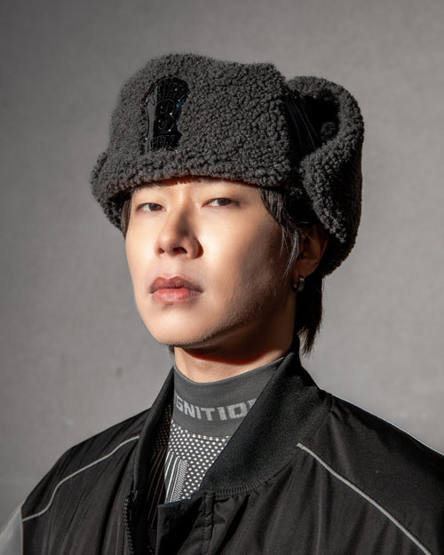 Person wearing a dark gray winter hat and black jacket against a gray background